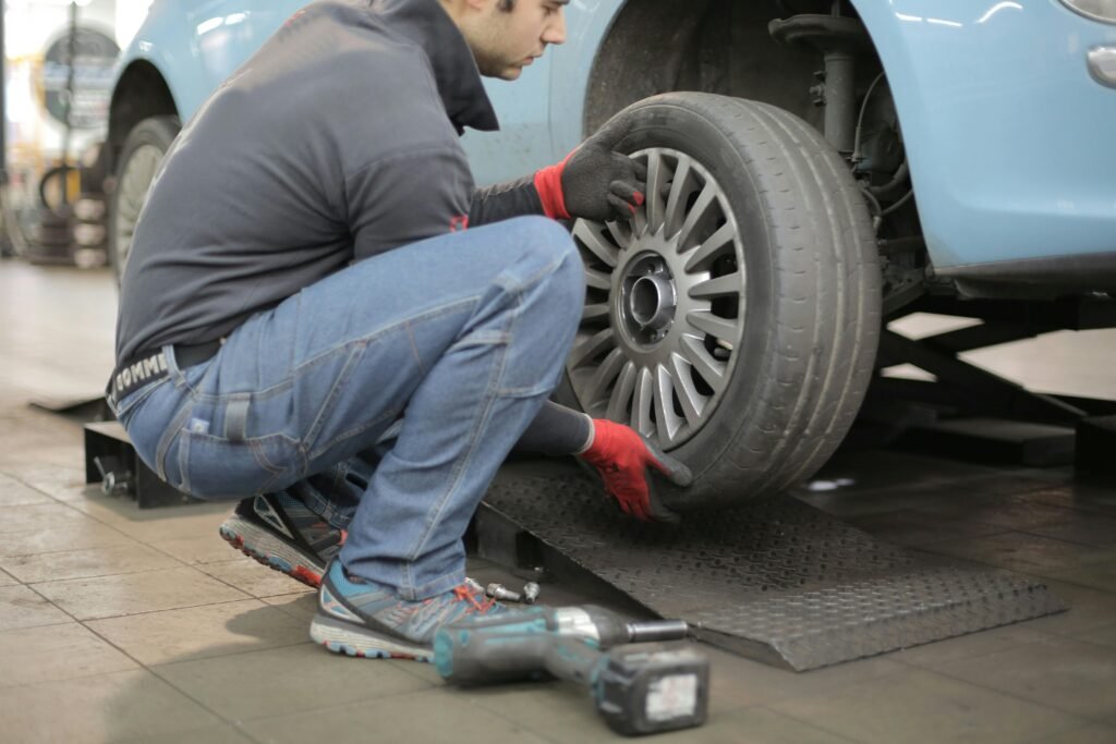 Mechanic changing a car tire indoors, using tools for vehicle maintenance.